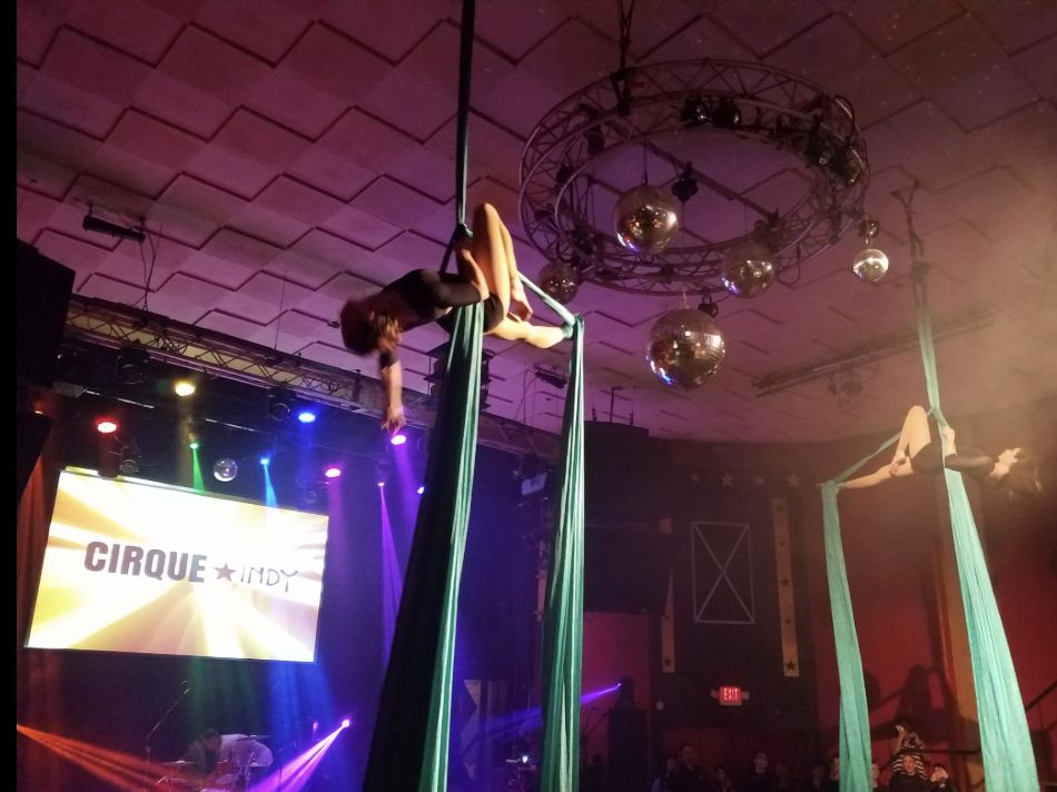Two aerialists performing on silks under stage lights